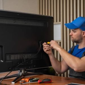 Master in blue T-shirt smiles after repairing TV set connector with screwdriver sitting at table. Diagnosis and repair of broken household appliances at home